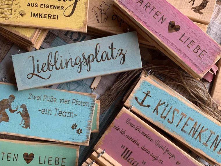 Ein Stapel fertiger Holzschilder mit verschiedenen Schriftzügen und Farbtönen
