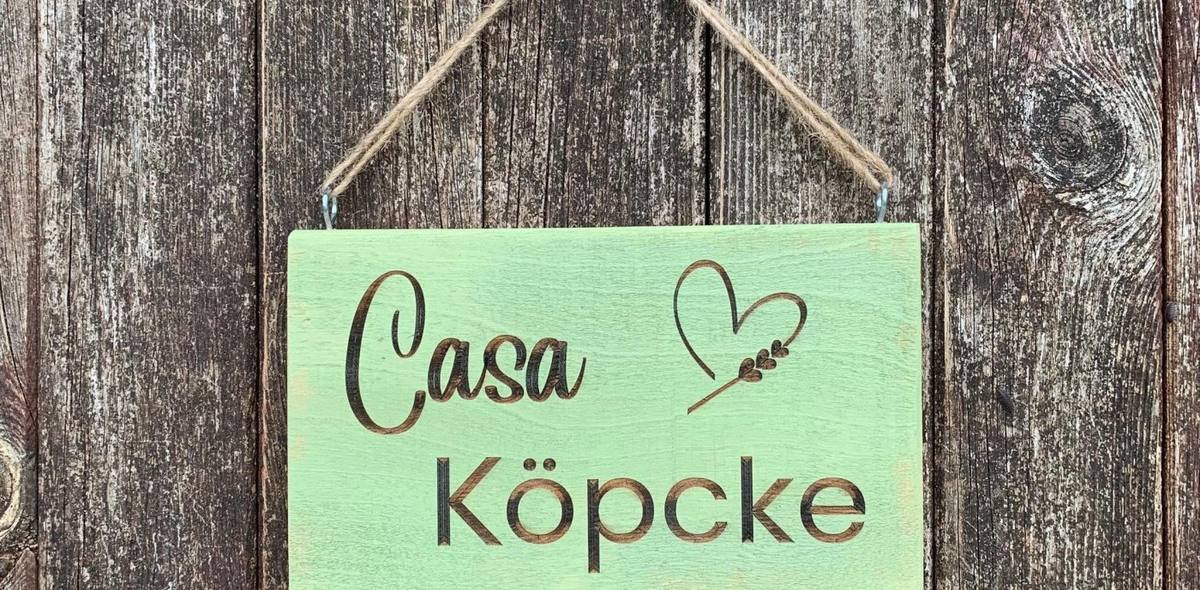 Grün gestrichenes Holzschild mit gebranntem Schriftzug Casa Köpcke und Herzmotiv