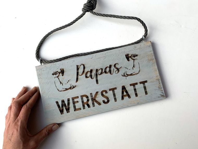Eine Hand hält ein graues Werkstattschild aus Palettenholz