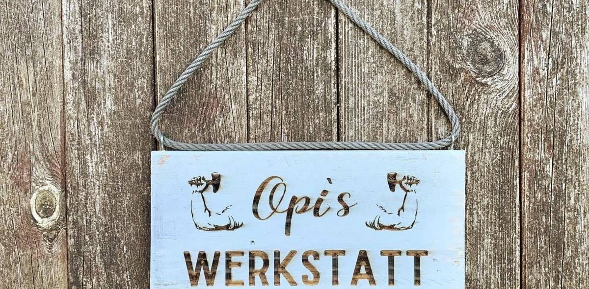 Hellblaues Holzschild an einer Sisalkordel vor einer verwitterten Bretterwand