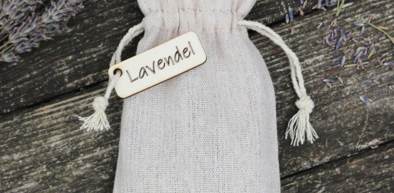Leinensäckchen mit Lavendel und Holzanhänger auf verwitterten Dielen