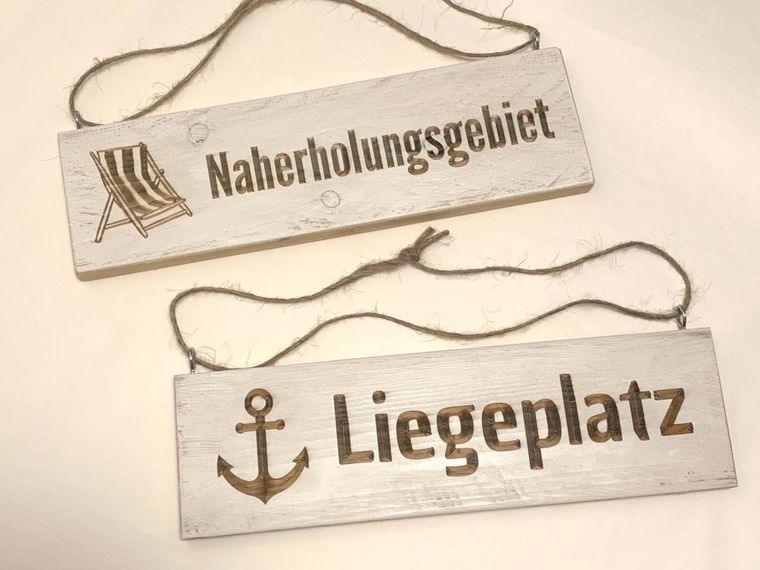 Zwei schmale Holzschilder mit den Schriftzügen Naherholungsgebiet und Liegeplatz, jeweils mit kleinem Motiv