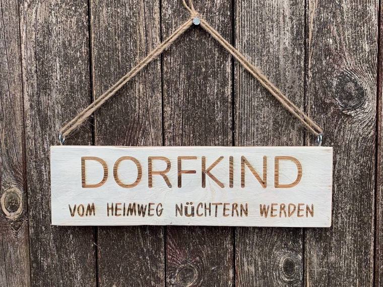 Helles Holzschild mit der Überschrift DORFKIND und der kleineren Unterzeile vom Heimweg nüchtern werden