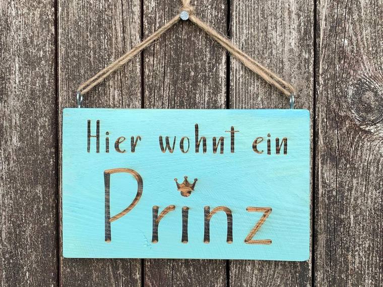 Türkisfarbenes Holzschild mit dem zweizeiligen Schriftzug Hier wohnt ein Prinz und einer kleinen Krone