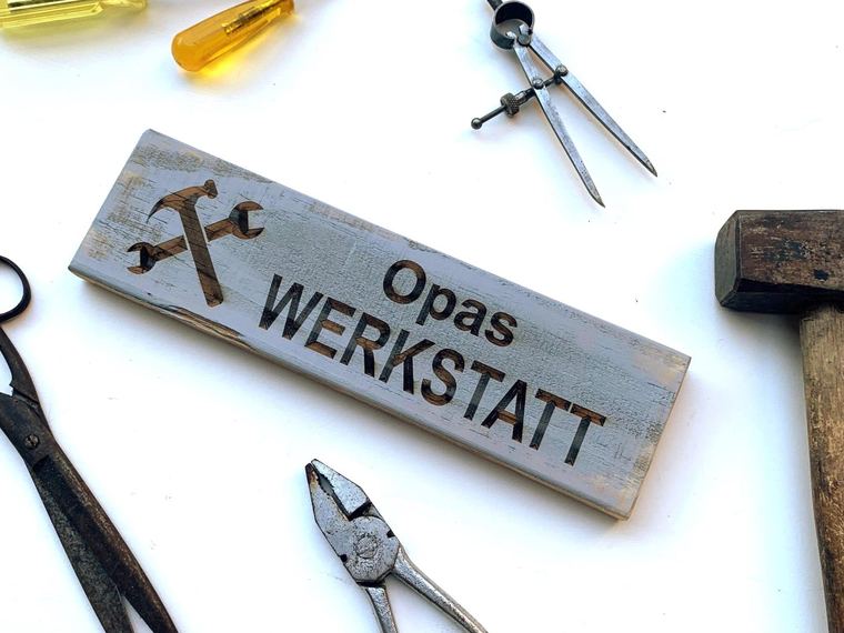 Werkstattschild aus Altholz zwischen Schraubendrehern, Zange, Blechschere und Zirkel